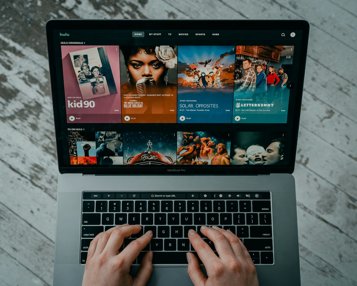 Hands typing on a laptop showing Hulu interface.